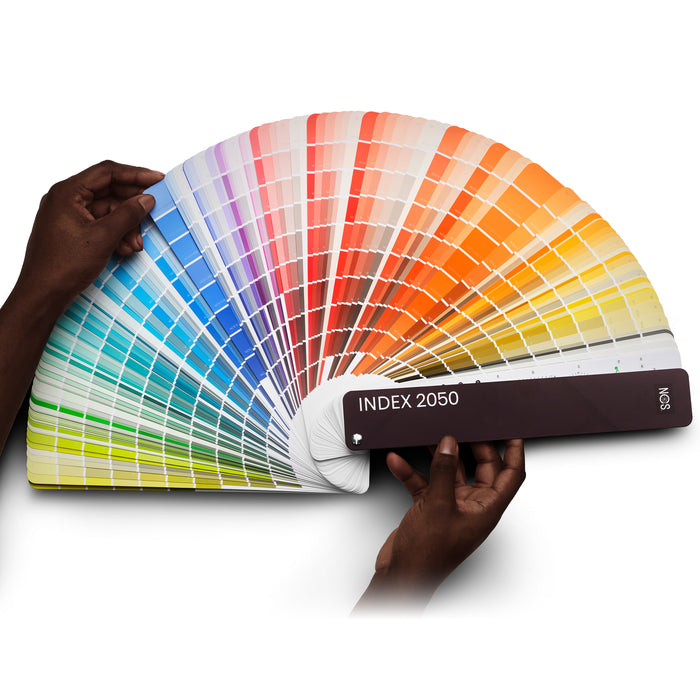 The NCS INDEX 2050 colour fan guide from the Natural Colour System, showing a person fanning the guide out to browse paper colour samples.
