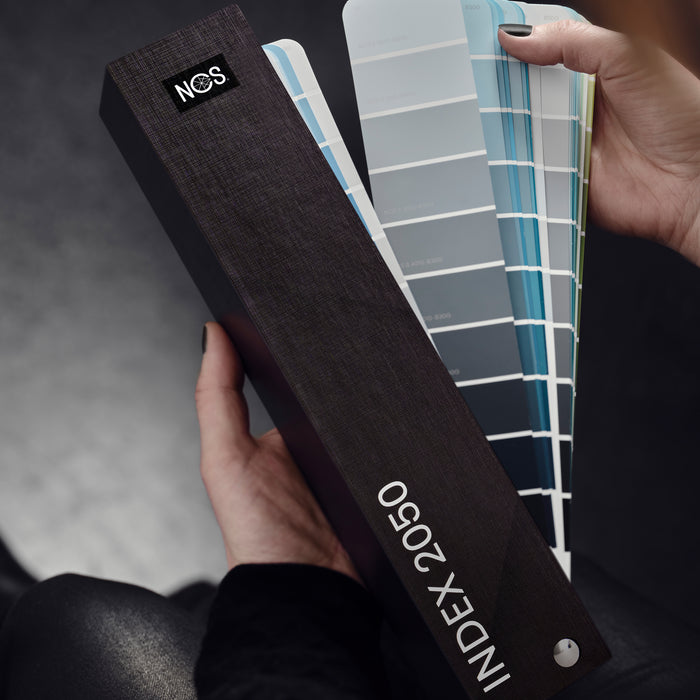 The NCS INDEX 2050 colour fan guide from the Natural Colour System, showing a person fanning the guide out to browse paper colour samples.