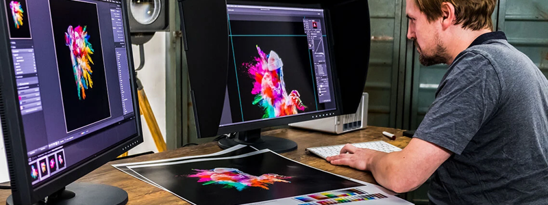 An image of a man working on some designs using two EIZO ColorEdge monitors and an EIZO shading hood.