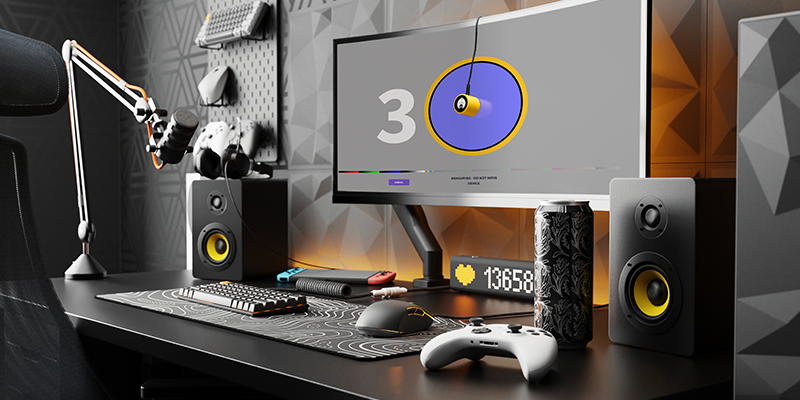 Gaming set up on a black desk with gaming consoles, controllers and a large curved monitor, showing a Calibrite Display 123 device being used to calibrate the colours on the monitor screen.